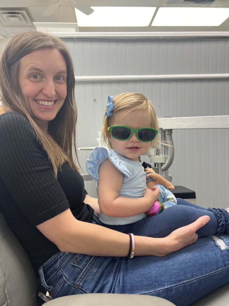 The image shows a woman holding a little girl wearing an eyeglasses.