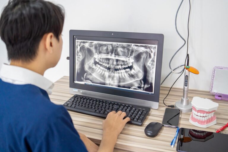 Rear view of a dentist watching a 3D image of jaw in laptop or computer monitor, using health technology concept.