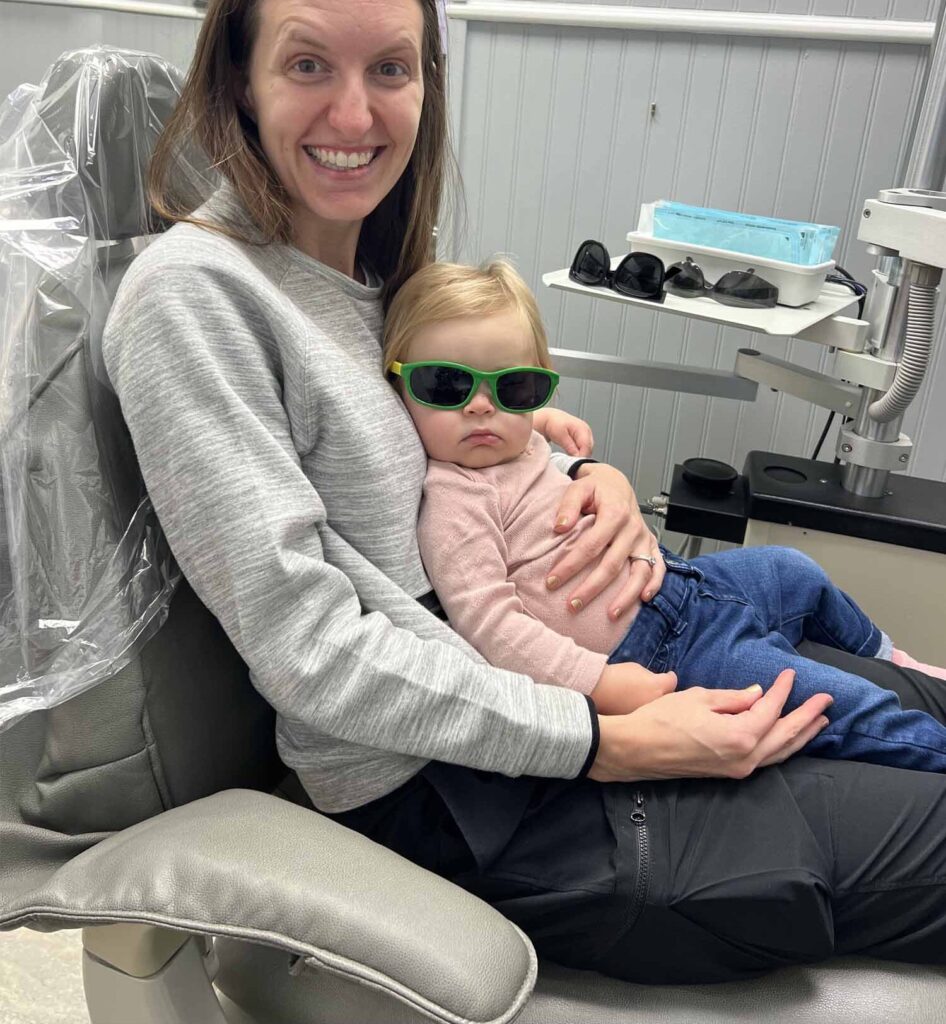 Dr. Fischman's wife with their baby, Lucy, wearing protective glasses while sitting on a patient chair for her first checkup