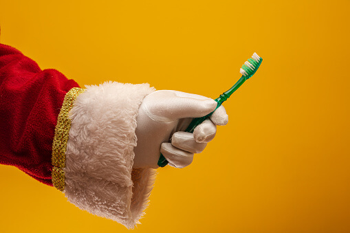 santas arm holding a toothbrush with a yellow background