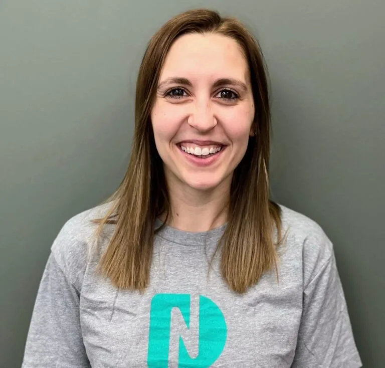 Headshot of Carlie a licensed Dental assistant wearing a shirt with a logo of Nebraska Dental, in a plain gray background.