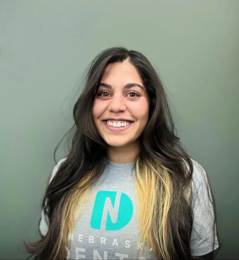 Headshot of Dana a front office administrator wearing a shirt with a logo of Nebraska Dental, in a plain gray background.