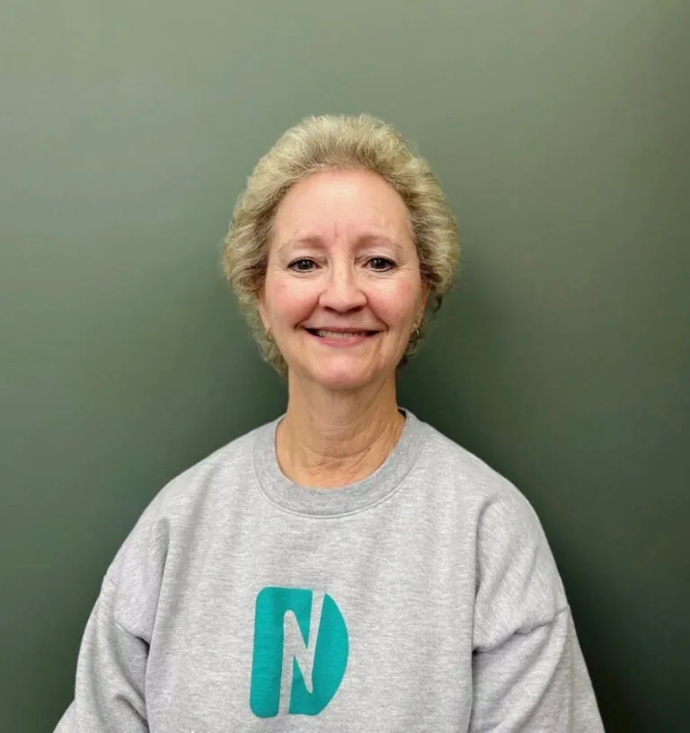 Headshot of Diane a receptionist wearing a shirt with a logo of Nebraska Dental, in a plain gray background.