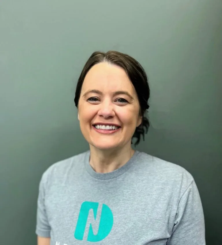 Headshot of Merry a dental hygienist wearing a shirt with a logo of Nebraska Dental, in a plain gray background.