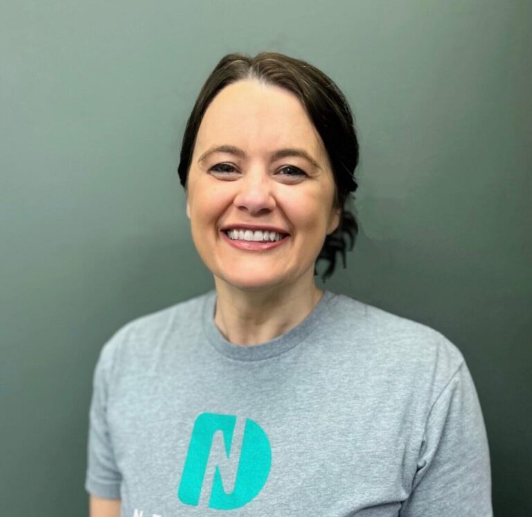 Headshot of Merry a dental hygienist wearing a shirt with a logo of Nebraska Dental, in a plain gray background.