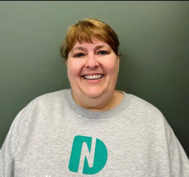 Headshot of Renee a certified dental assistant wearing a shirt with a logo of Nebraska Dental, in a plain gray background.